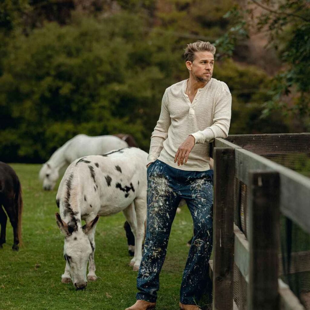 Charlie Hunnam posing beside horses on a ranch in casual clothing